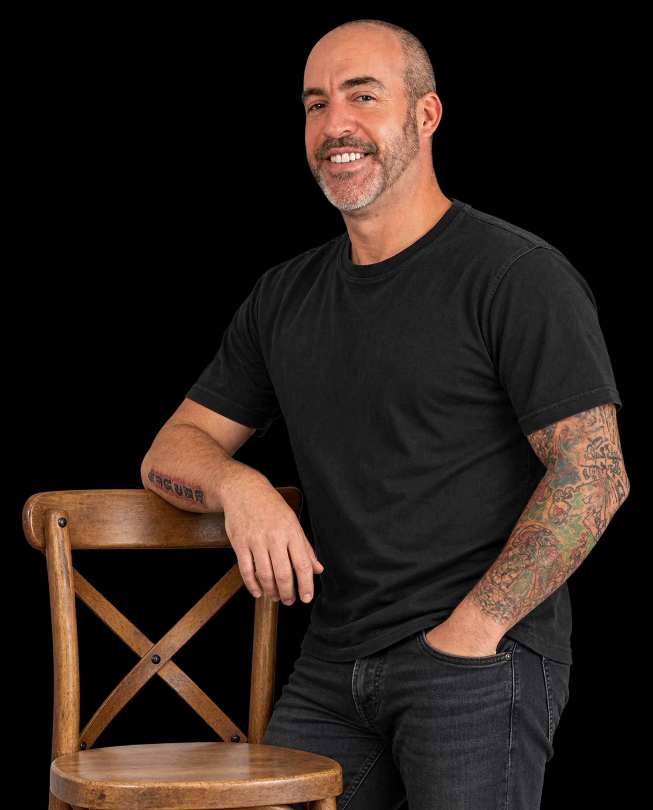 Adam Godsall in a relaxed black T-shirt, leaning on a wooden chair